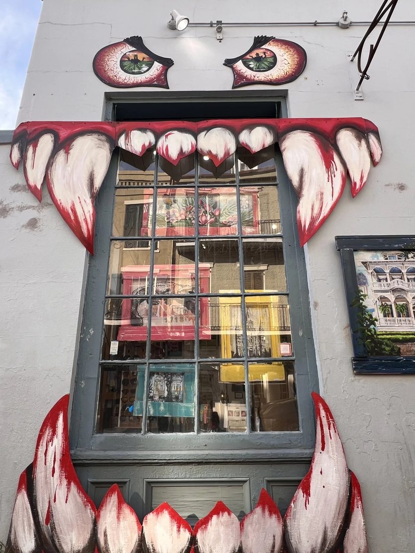 A white building wall where a window is painted as a monster face, with big eyes above and red-tipped fangs around the frame.